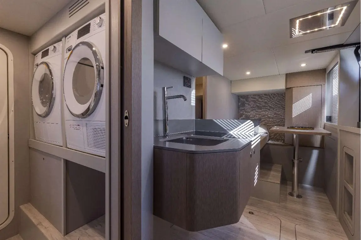 A modern utility area featuring stacked white washer and dryer, a sleek grey sink, and ambient lighting in a compact space.